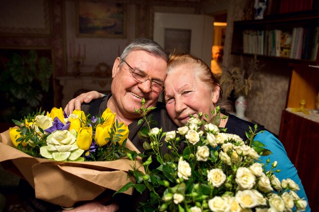 Großvater mit Blumensträußen gratuliert Großmutter. Älteres verliebtes Paar. Rentner küssen sich. Familie im Ruhestand.