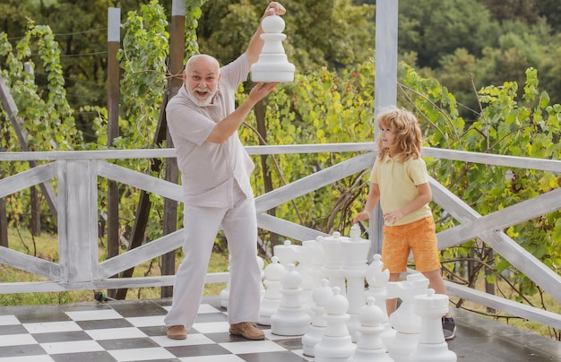 Großvater und Enkel spielen Schach auf einem großen Schachbrett älterer alter Verwandter mit Kind