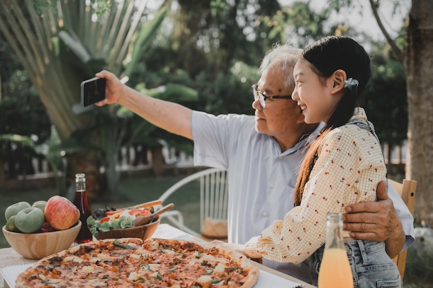 Großvater und Enkelin beim Abendessen im Garten zu Hause. Lebensstil im Rentenalter mit der Familie im Sommerurlaub.