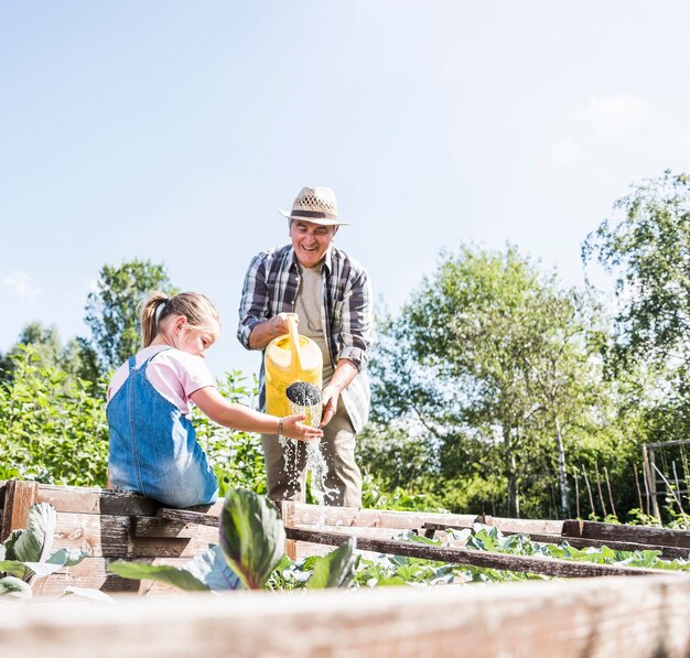 Foto großvater und enkelin im garten, die pflanzen gießen