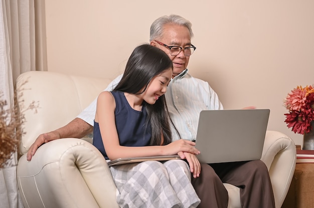 Großvater und Enkelin lernen online zu Hause. Lebensstil im Rentenalter mit der Familie im Sommerurlaub.