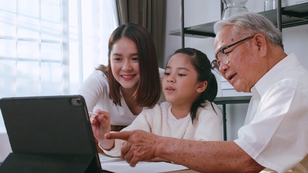 Großvater und Mutter unterrichten Tochter Hausaufgaben, während sie zu Hause online lernen.