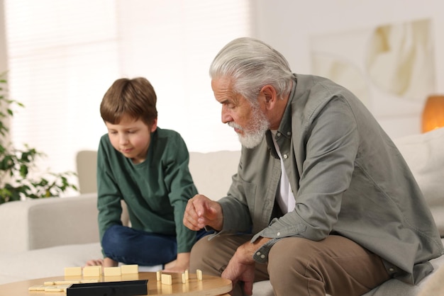 Großvater und sein Enkel spielen Domino an einem Tisch im Innenraum