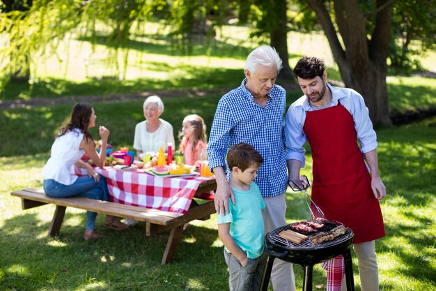 Großvater, Vater und Sohn grillen im Park