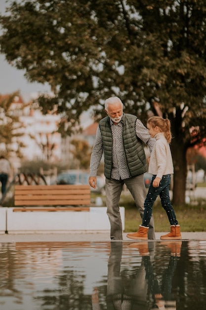 Großvater verbringt am Herbsttag Zeit mit seiner Enkelin am kleinen Wasserbecken im Park