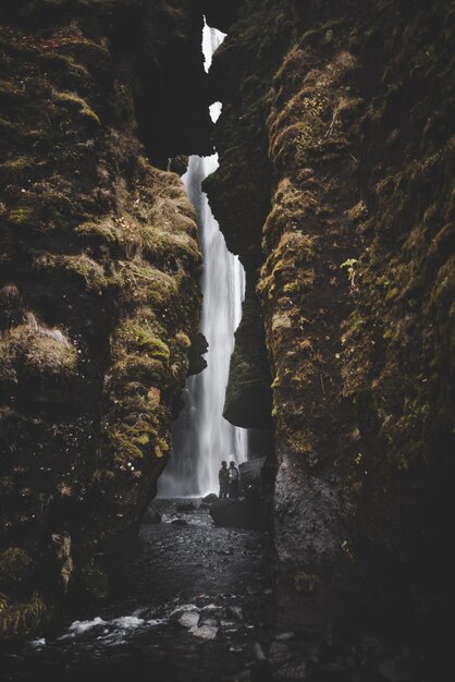 Foto grotte eines wasserfalls in island mit moosbedeckten wänden und zwei personen im hintergrund am wasser