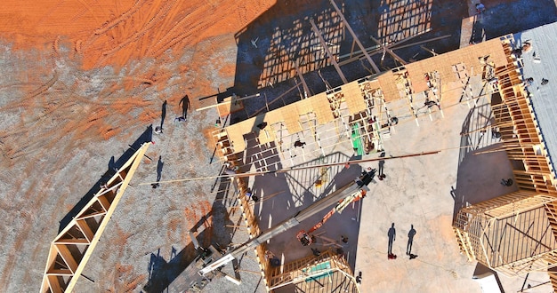 Una grúa aérea vista desde arriba sostiene vigas de techo de madera en el edificio superior de una nueva casa de madera bajo construcción