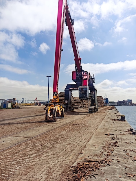 Grúa con cuchara de agarre en el muelle para cargar madera en los barcos en el puerto