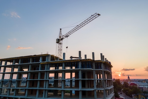 Grúa de elevación de torre y alto edificio de apartamentos residenciales con marco monolítico en construcción al atardecer Desarrollo inmobiliario