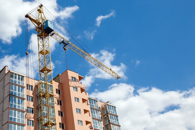 Grúa que construye el nuevo edificio de apartamentos moderno en un fondo del cielo nublado azul en el día soleado.