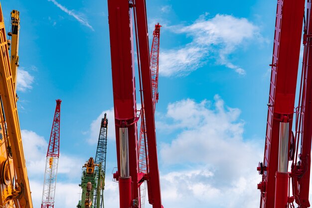 Grúa sobre orugas contra el cielo azul y las nubes blancas. Sector inmobiliario. La grúa sobre orugas roja utiliza el equipo de elevación del carrete en el sitio de construcción. Se alquila grua. Concesionario de grúas para empresas de construcción.