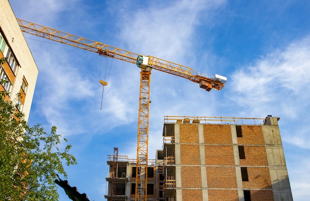 Grúa torre de construcción en el sitio de construcción de un edificio residencial de ladrillo moderno contra el fondo de la luz del sol amanecer verano