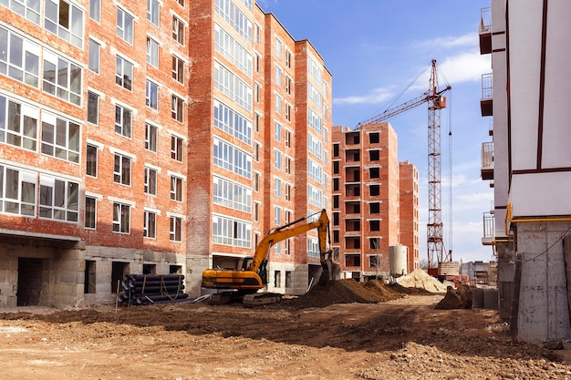 Grúa torre y excavadora cerca de un edificio de gran altura sobre un fondo de cielo nublado