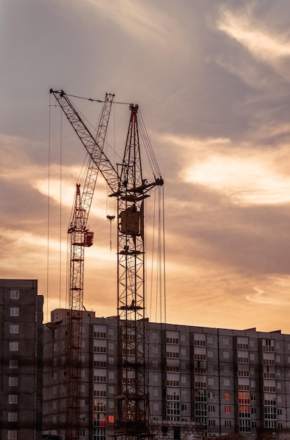 Grúa torre en un sitio de construcción al amanecer con un fondo de cielo nublado Construcción de edificios modernos de gran altura Construcción de casas de apartamentos en nuevas áreas