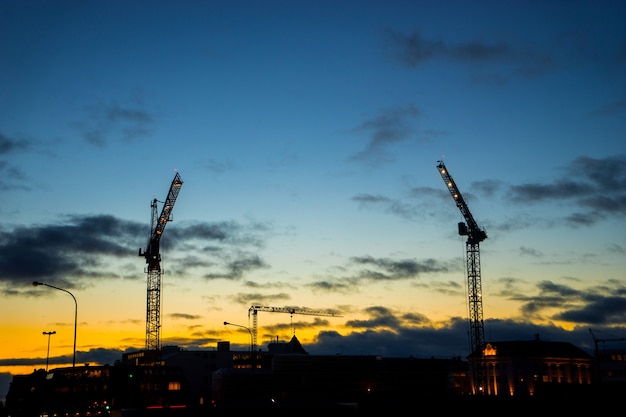 Grúas de construcción industrial y siluetas de edificios sobre el sol al amanecer.