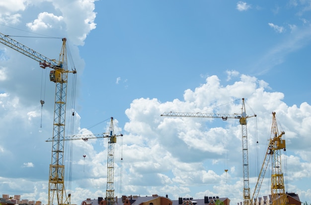 Grúas de construcción sobre fondo azul cielo nublado en un sitio en construcción