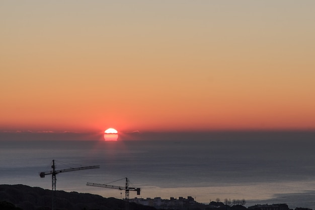 Grúas de obras a contraluz con amanecer de fondo