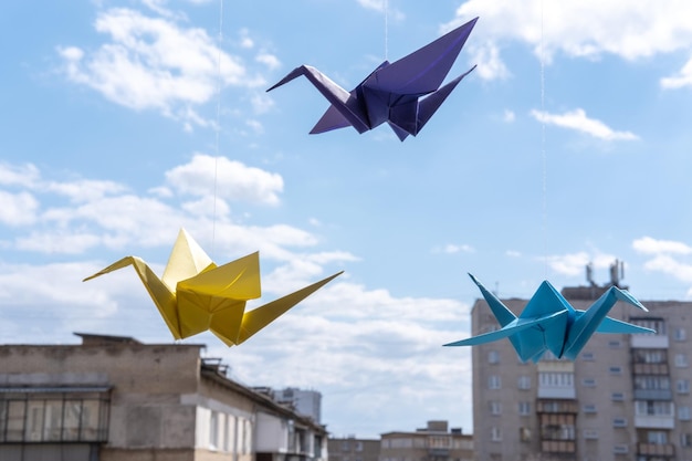 Grúas de pájaros de origami de papel multicolor colgando de la ventana contra el fondo del cielo Grúa de origami