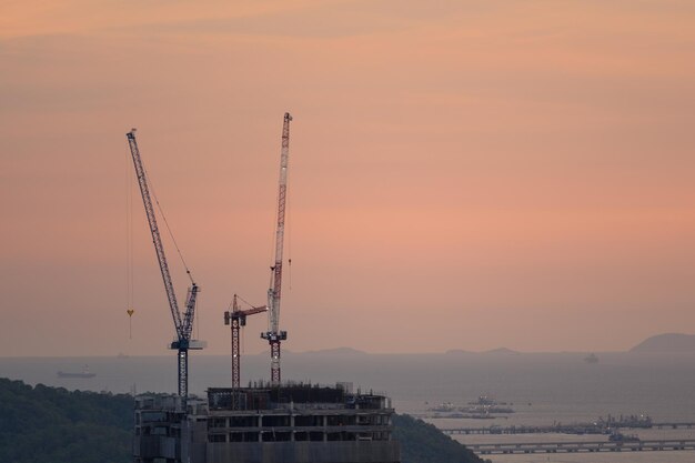 Las grúas son bloques de construcción a lo largo de la costa al atardecer. Construcción con grúa al atardecer en el muelle. Construcción de grúa