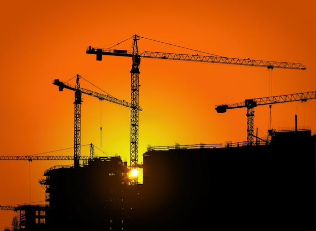 Grúas torre y silueta de edificio con trabajadores al amanecer.