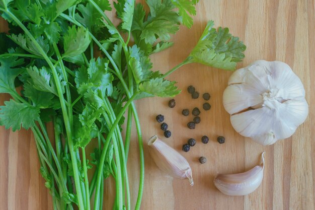 Grün verlässt Koriander oder Koriander, Knoblauch und schwarzen Pfeffer setzen auf Holztisch