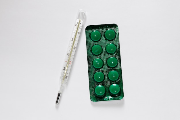 grüne Blase mit Pillen und Thermometer auf einer weißen Oberfläche