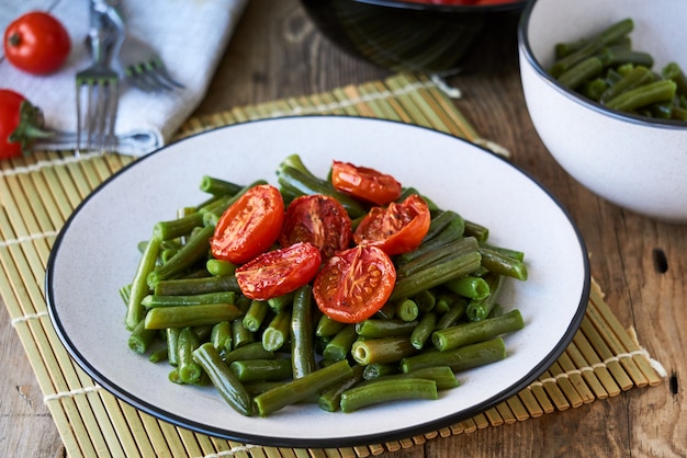 Grüne Bohnen mit gebackenen Kirschtomaten auf einem Holztisch