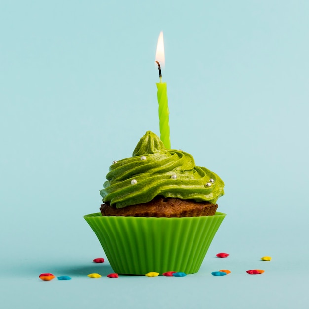 Foto grüne brennende kerzen auf dekorativen muffins mit buntem stern besprüht gegen blauen hintergrund