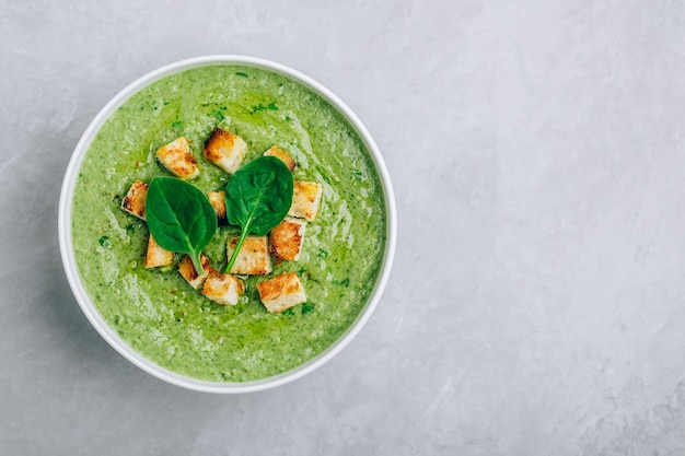 Grüne Cremesuppe Cremige Spinat-Brokkoli-Suppe mit Croutons auf grauem Steinhintergrund Draufsicht mit Kopierbereich