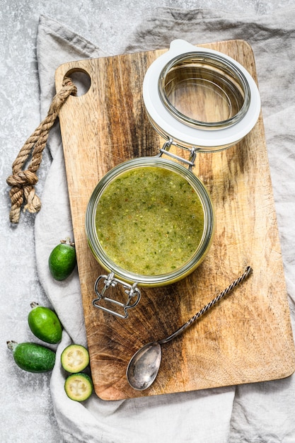 Grüne Feijoamarmelade auf einem hölzernen hackenden Brett in einem Glasgefäß.