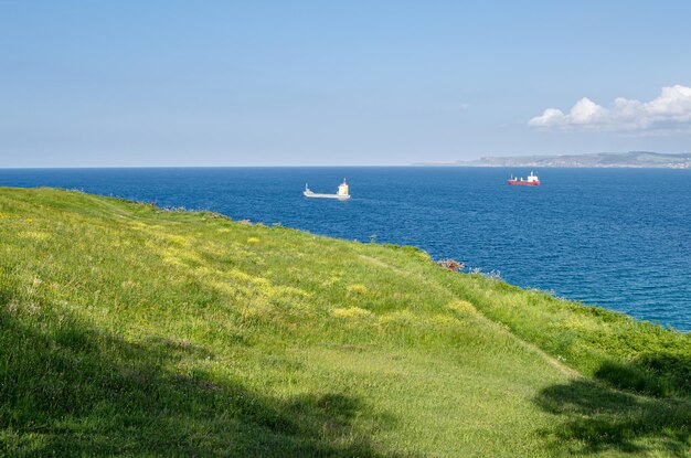 Grüne felsige Küste von Santander mit Booten im Hintergrund