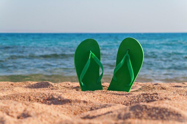 Grüne Flipflops im Sand am Meer