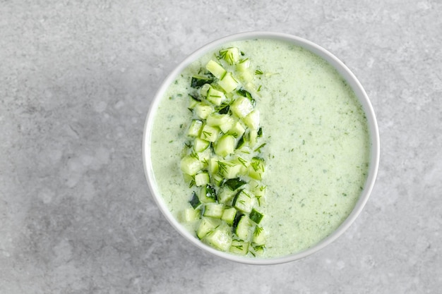 Grüne frische kalte Sommersuppe verziert mit Gurkenstücken auf Draufsicht des grauen Hintergrundes