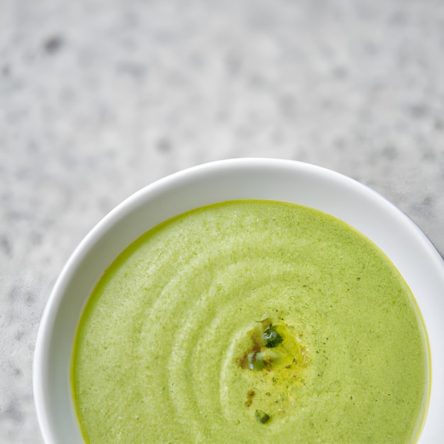 Grüne Gemüsecremesuppe in einer weißen Schüssel auf grauem Betonhintergrund, Draufsicht, veganes Suppenpüree