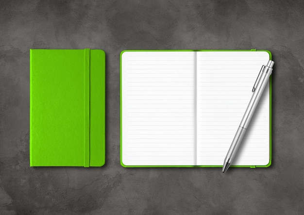Grüne geschlossene und offene Notizbücher mit einem Stift auf Betontisch.