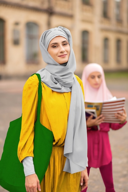 Grüne Handtasche. Stilvolle muslimische Frau mit hellgrüner Handtasche, die draußen in der Nähe eines Freundes steht