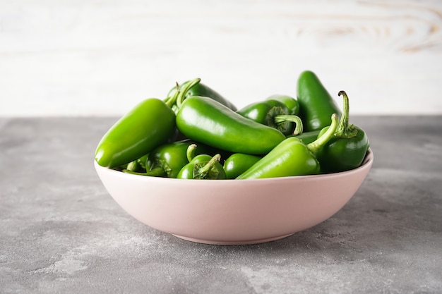 Grüne Jalapenopfeffer in einer Pastellplatte auf grauem Hintergrund.