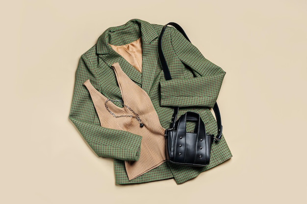 Grüne klassische Jacke und beiges Damenoberteil mit Handtasche. Trendige Herbst- oder Frühlingskleidung für Damen. Modekonzept. Flache Lage, Draufsicht.