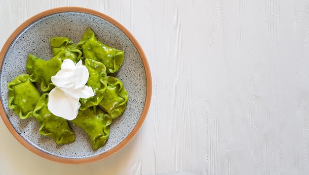 Grüne Knödel mit Quark, Spinat und Sauerrahm auf Keramikplatte auf weißem Hintergrund. Horizontal, Draufsicht, mit Kopierbereich.