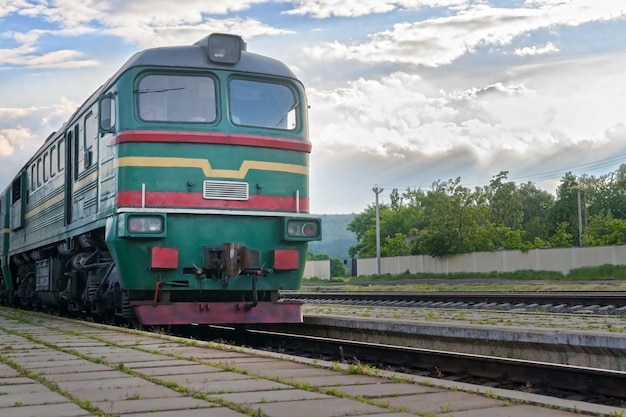 Grüne Lokomotive kommt am Bahnhof vor dem Hintergrund eines stürmischen Himmels an