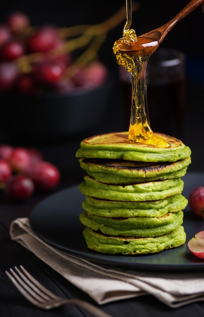 Grüne Pfannkuchen mit Matcha-Tee oder Spinat, gekleidetem Honig und roten Trauben. Ideen und Rezepte für ein gesundes Frühstück mit Superfood-Zutaten. Dunkler Hintergrund