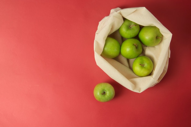 Grüne Äpfel in der weißen Einkaufstasche, roter Hintergrund. Null-Abfall-Konzept.