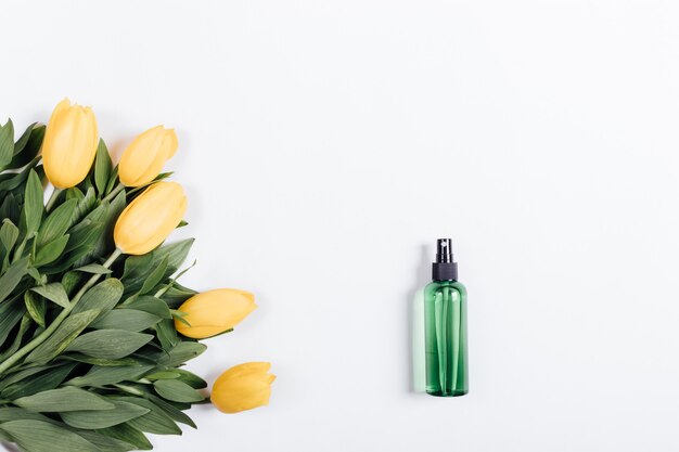 Grüne Plastikflasche mit Wasser und einem Blumenstrauß von gelben Tulpen auf einem weißen Hintergrund