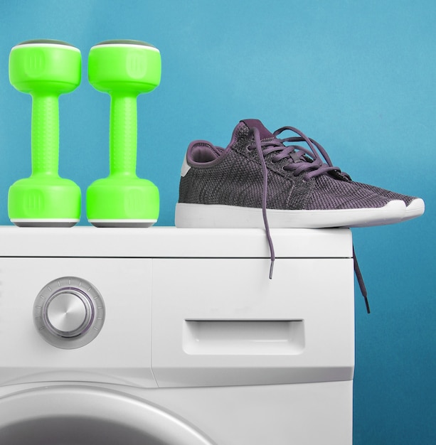 Grüne Plastikhanteln, Sportschuhe auf Waschmaschine gegen blauen Hintergrund