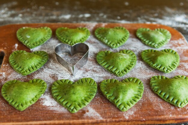 Grüne Ravioli in Herzform auf Holzunterlage