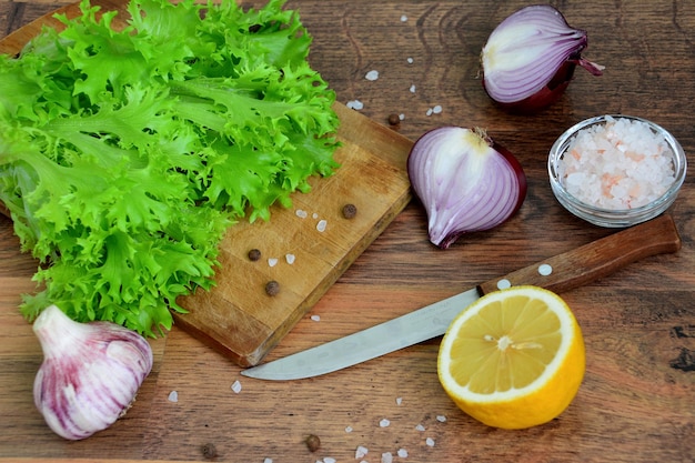 grüne salatblätter auf schneidebrett mit küchenmesser, spanischer zwiebel, zitrone, salz und knoblauch