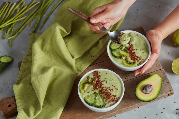 Grüne Smoothie-Schüssel mit Avocado-frischer Kiwi und grüner Gurke in den Händen auf Steinhintergrund