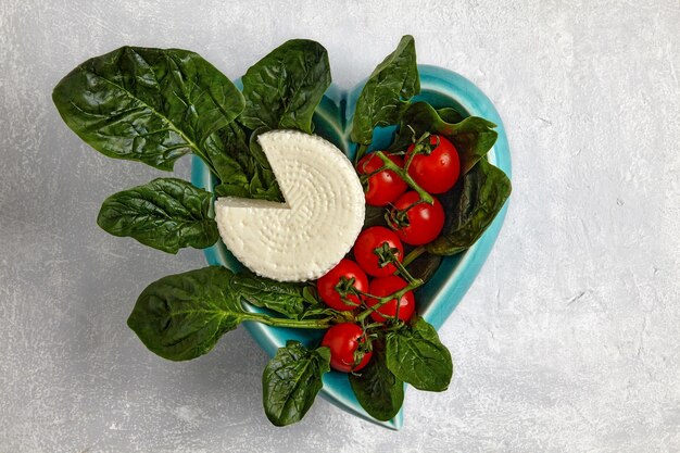 Grüne Spinatblätter und Mozzarella-Quark auf einem dunklen Teller auf einem hellen Betontisch