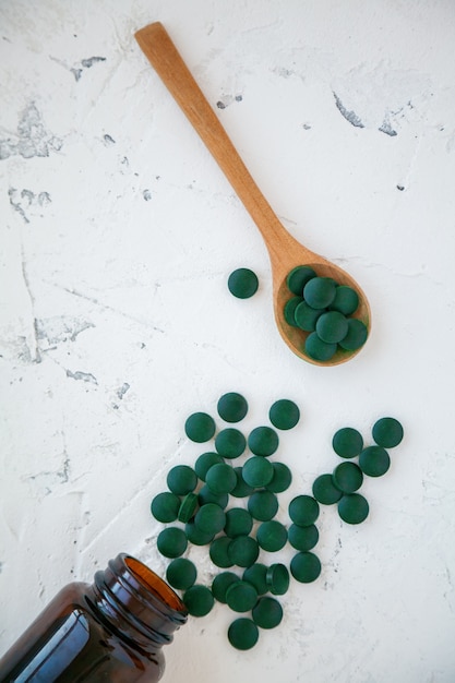 Grüne Spirulina-Pillen fielen aus der Flasche. Mehrere Pillen in einem Holzlöffel. Super Food Konzept. Spirulina Nahrungsergänzungsmittel.