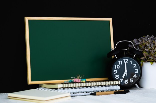 Grüne Tafel mit Stapel Notizbücher und Wecker